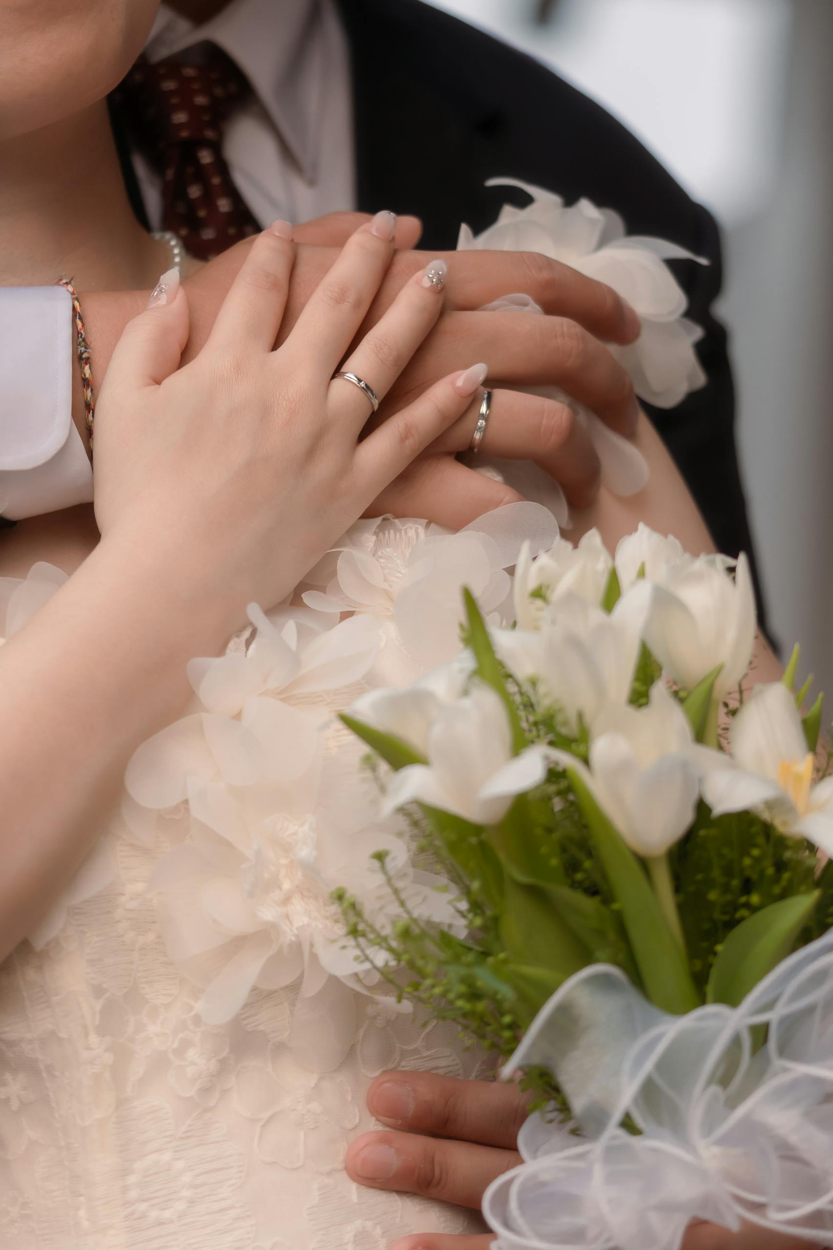 Close-up of a newlywed couple embracing, showcasing wedding rings and a floral bouquet.