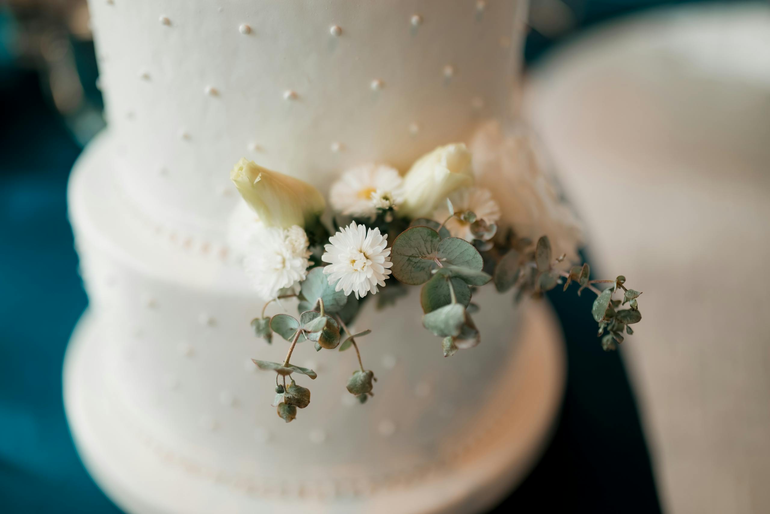 Close-up of a white wedding cake adorned with delicate floral decorations and soft pastel tones.