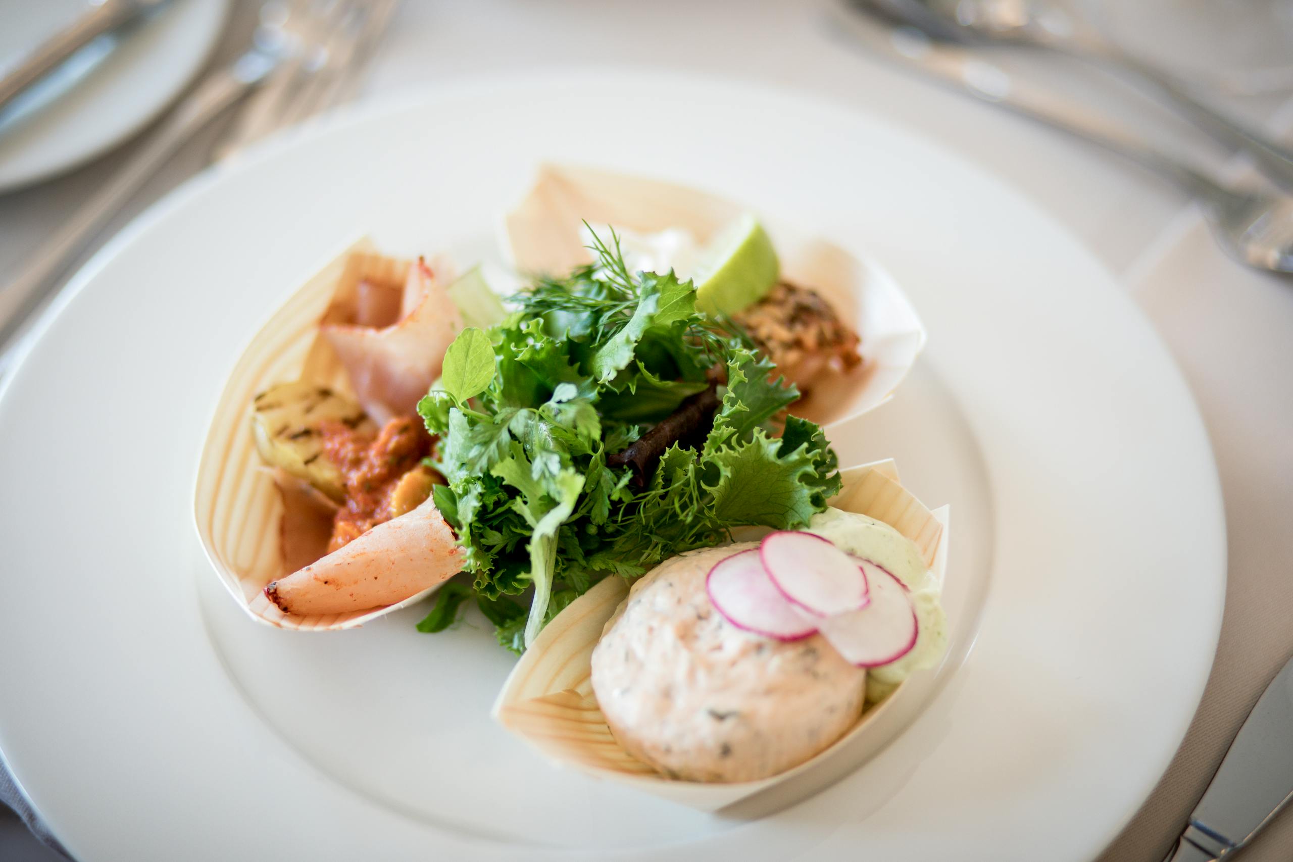 Elegant presentation of gourmet dish with greens, radish, and dips on a plate.