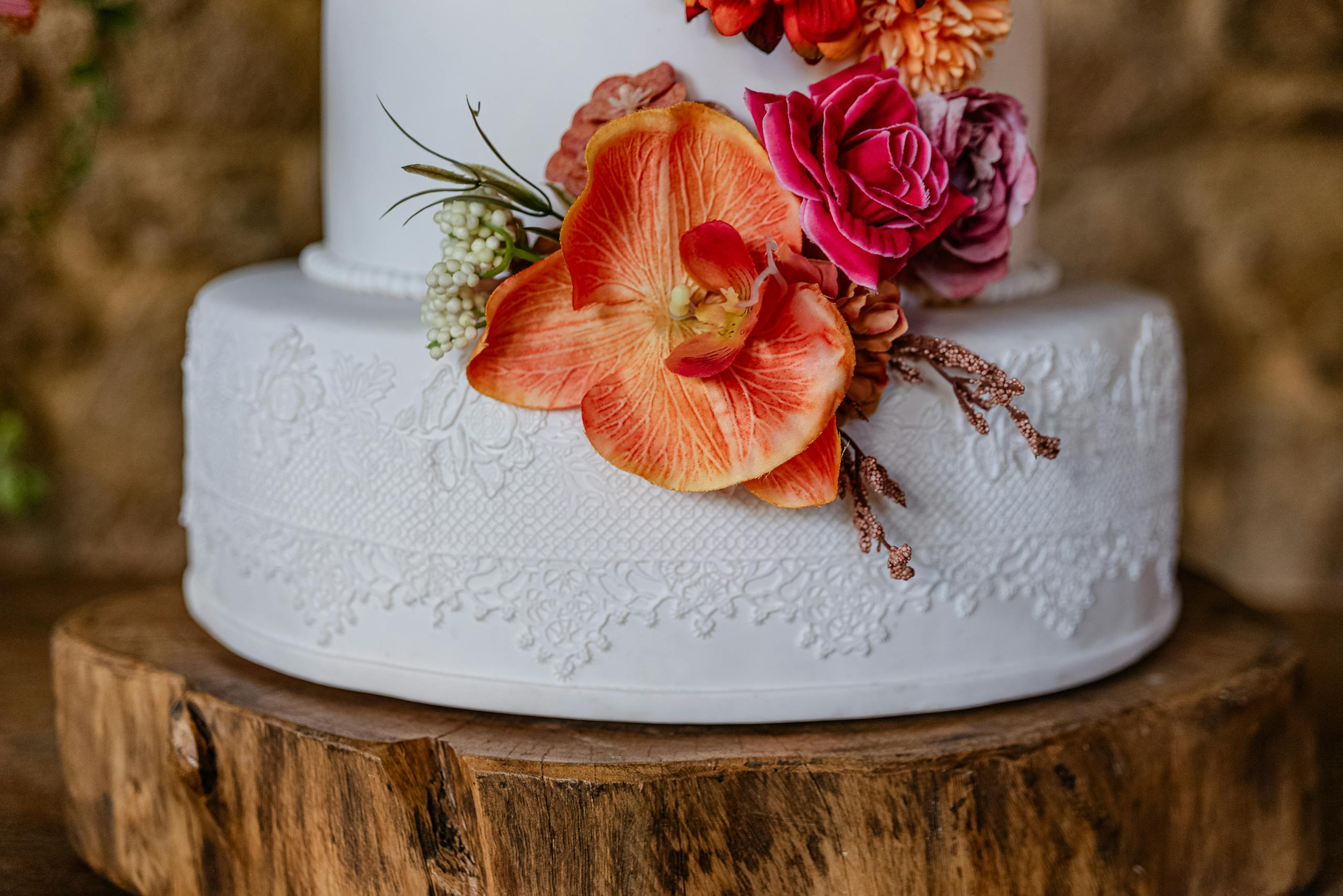 Elegant white wedding cake adorned with vibrant flowers on a rustic wooden stand.